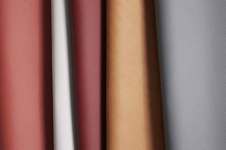 A leather-like material in various colors such as red, grey, and natural leather draped over each other with a visible grain texture visible on the surface of the material.
